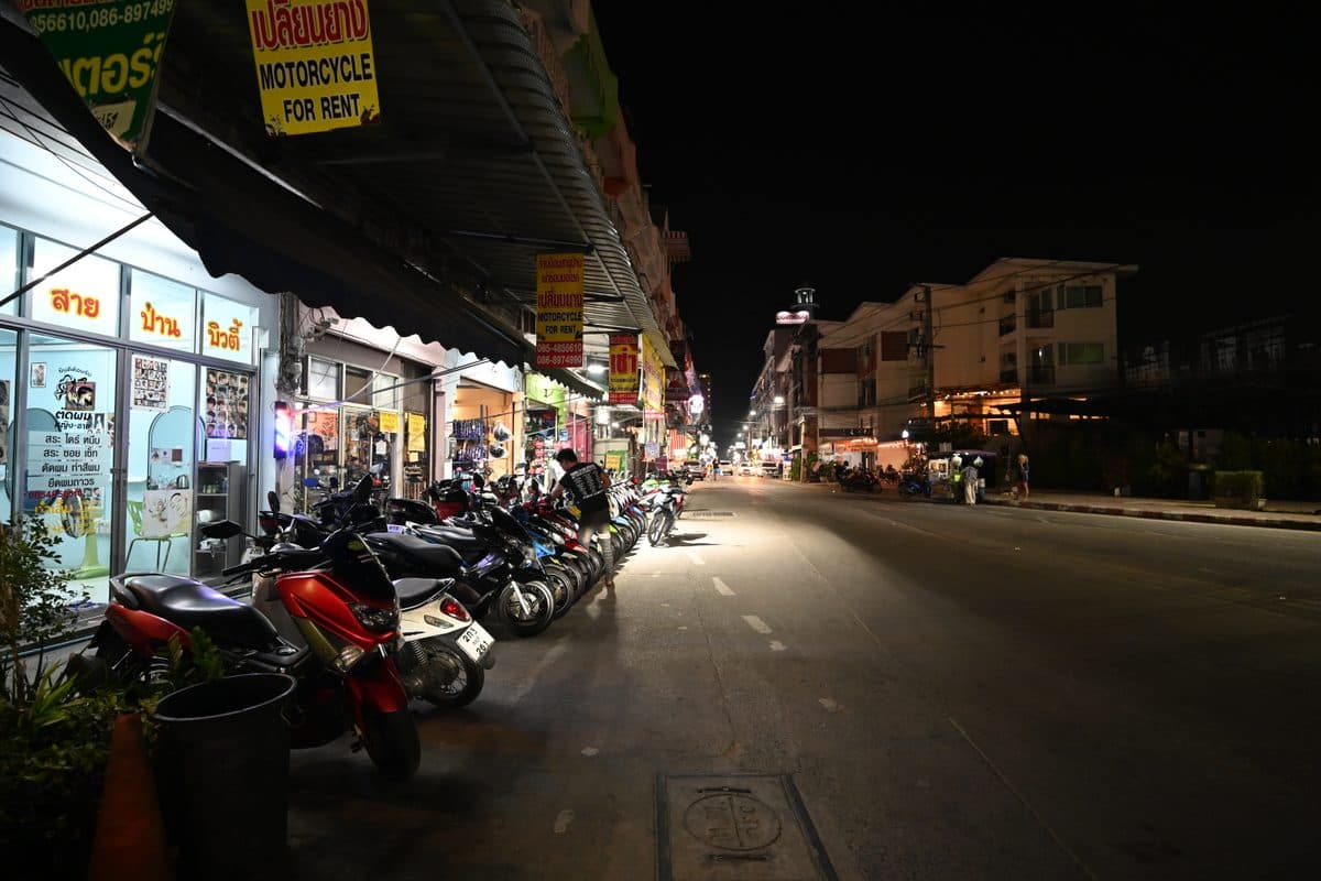Ряд припаркованных байков напрокат под вывеской 'Motorcycle for Rent' на улице Пхукета вечером