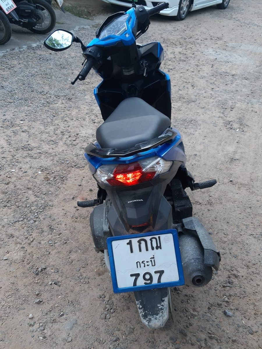 Honda Click 125 синего цвета, вид сбоку, припаркован среди других скутеров в Таиланде.